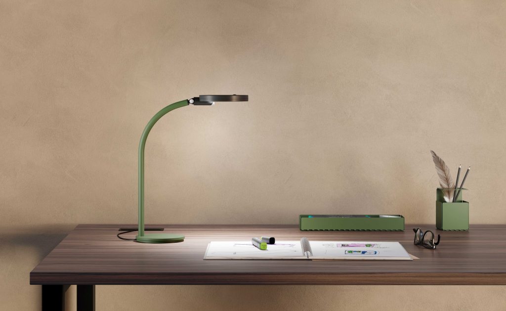 Simple image with a desk on which various elements are placed, including a flexible green desk lamp.