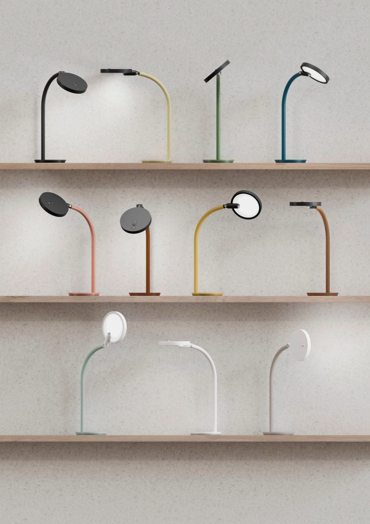 Image of a gray wall with three shelves where several desk lamps of different colors are installed.