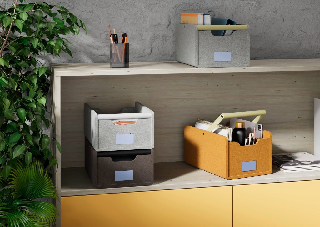 Armoire ouverture avec un panier de rangement gris en feutre PET et poignée bois sur le dessus. Sur l'étagère en dessous, il y a deux paniers de rangement en feutre PET superposés. Puis un autre panier de rangement en feutre PET jaune à côté. Dans chacun des paniers de rangement, il y a différents éléments/objets.