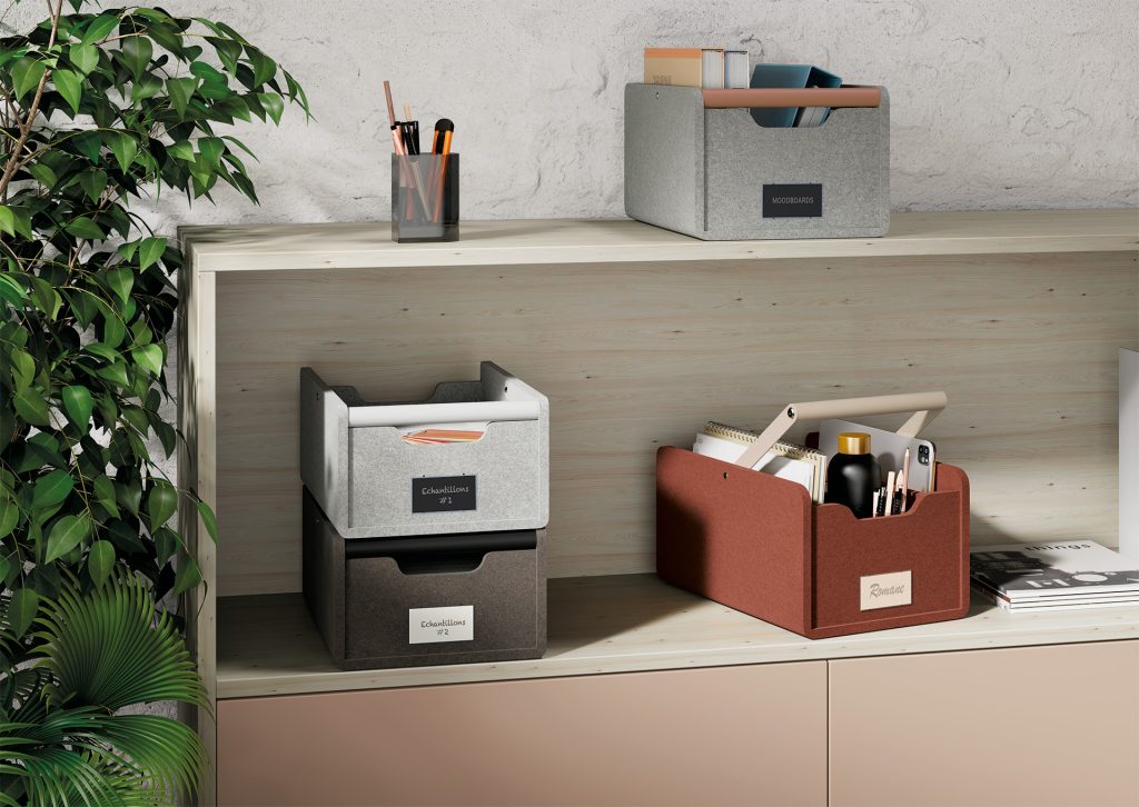 An opening cabinet with a gray PET felt storage basket and a wooden handle on top. On the shelf below, there are two PET felt storage baskets one on top of the other. Next to them is another PET felt storage basket. Each storage basket contains different items/objects.