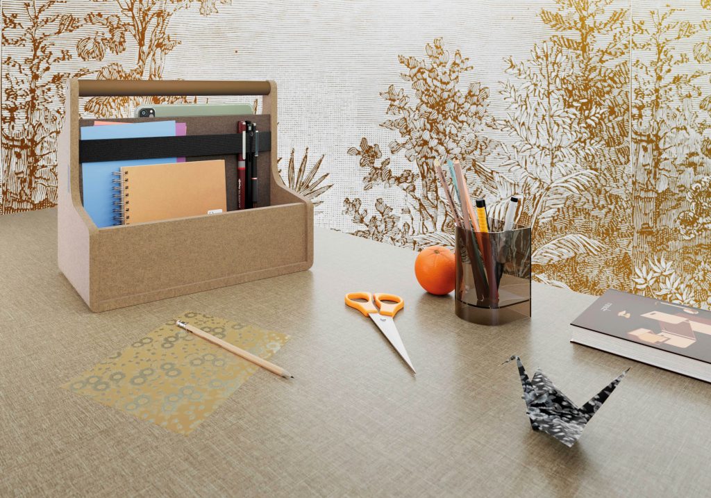 Bureau sur lequel est posé plusieurs éléments donc une toolbox en feutre PET de couleur brun clair avec poignée thermolaqué de couleur bronze.